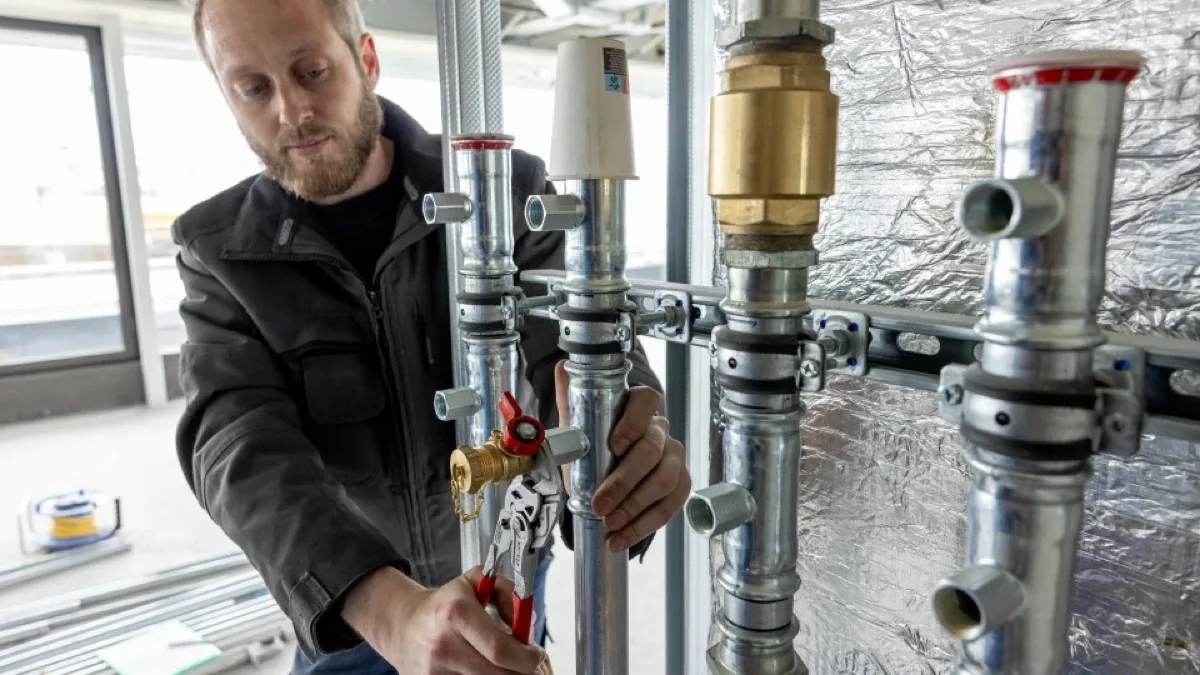 HVAC installer assembling galvanized metal pipework in a commercial building