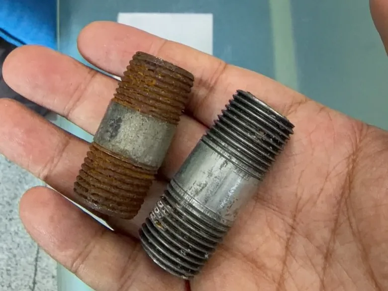 Hand holding two pipe nipples after about six months side by side: the cut-thread nipple is rusted at the threads while the rolled-thread nipple is still intact